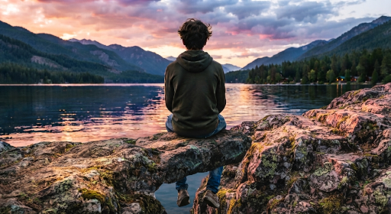 Adolescente sentado frente a un lago al atardecer